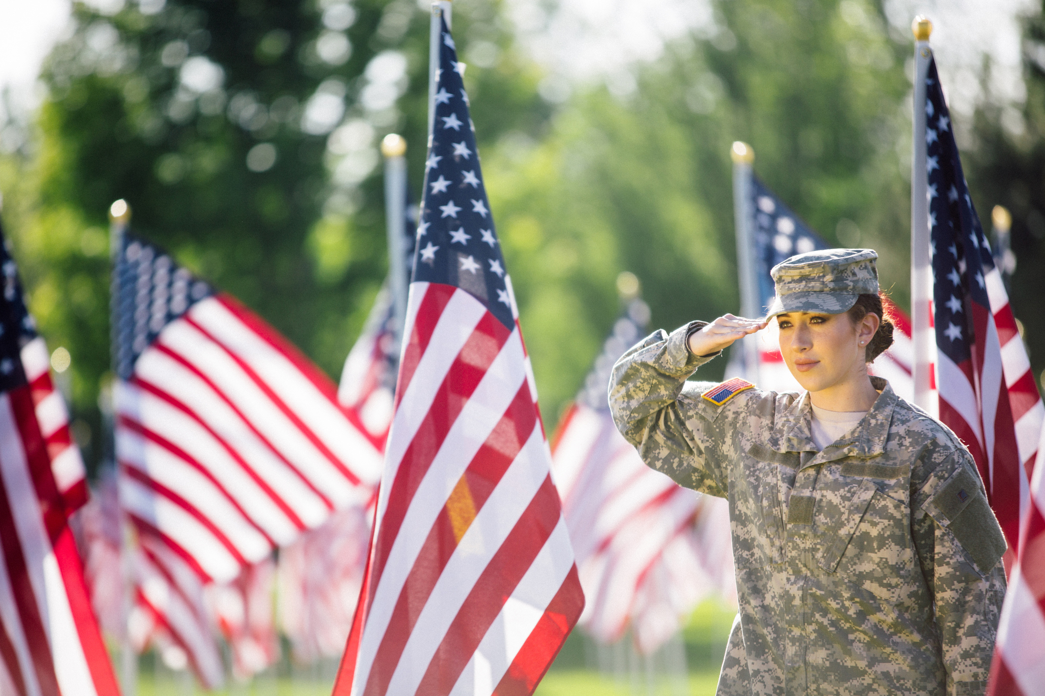 A young service woman salutes amid a field of American flags.